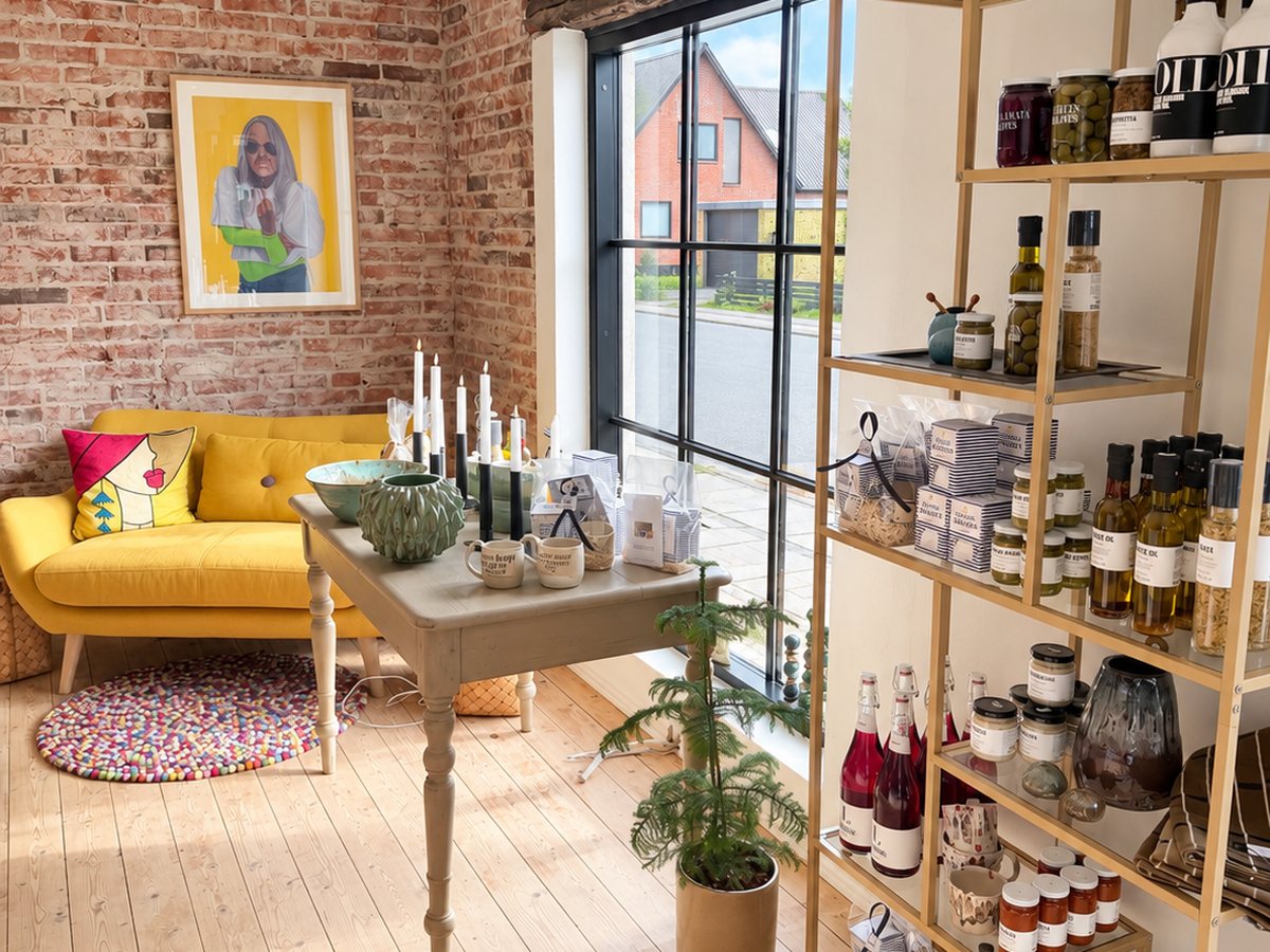 Butikken med guldreol fyldt med olie, oliven og delikatesser, et bord med keramik og den gule sofa